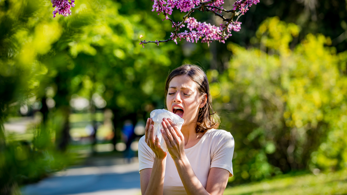 Woman outside holding a tissue about to sneeze into it